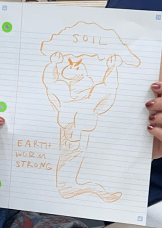 [A photo of a worm re-turning soil drawn by a workshop participant. This worm is drawn to have strong, human-like features, and lifts up a mound that is labeled SOIL. Written text next to it says: EARTH WORM STRONG.