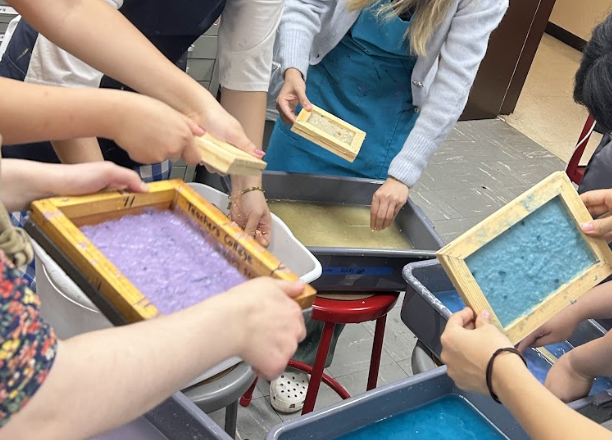 [A photo of hands moving in pulps. Hands are dipping mold and deckles into the tubs to make paper sheets.]