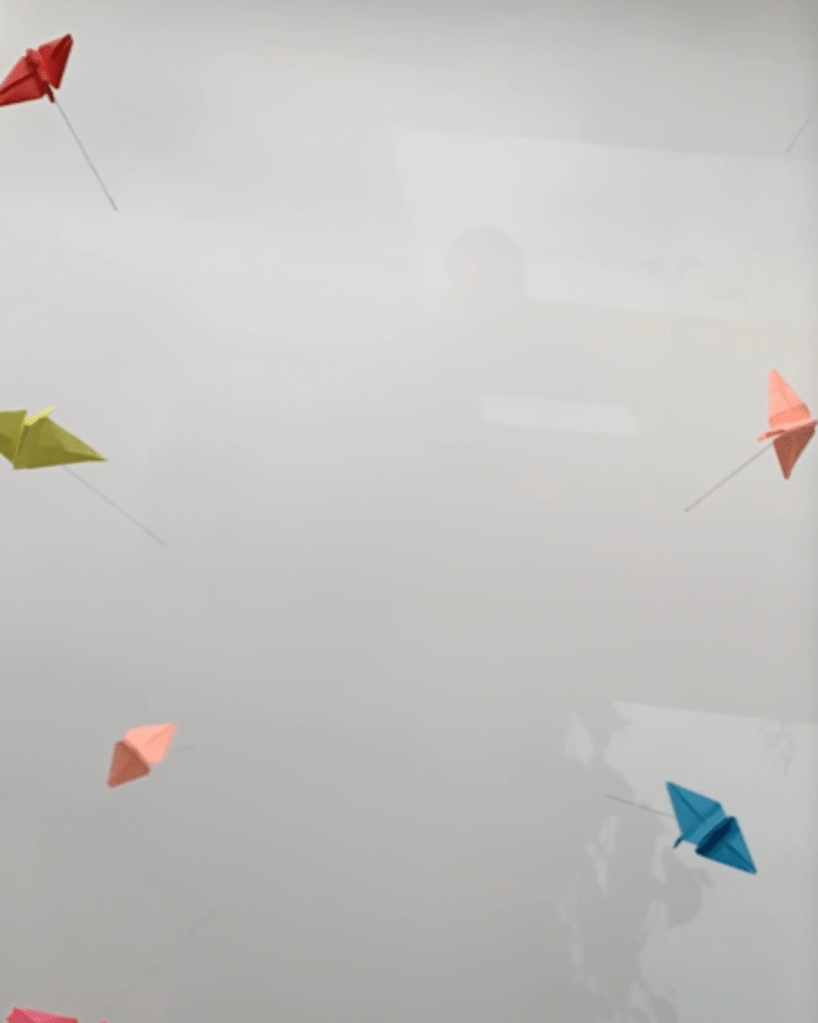 [This is a color photo of paper cranes, floating in the sky. ]
