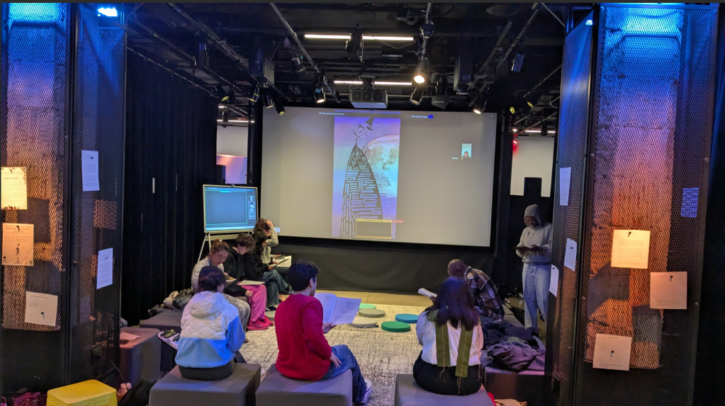 [a photo of participants gathered around Alana and Fred reading together from their play.]